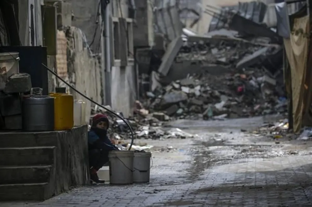 Un niño llena un cubo con agua entre los escombros de estructuras destruidas durante una operación militar israelí en el campo de refugiados de Al Nusairat, en el sur de la Franja de Gaza, 19 de febrero de 2024. Foto: EFE