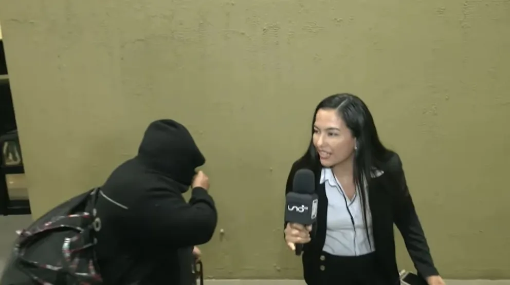 Uno de los pasajeros cubre su rostro mientras una periodista intenta obtener una declaración. Foto: Captura de video.