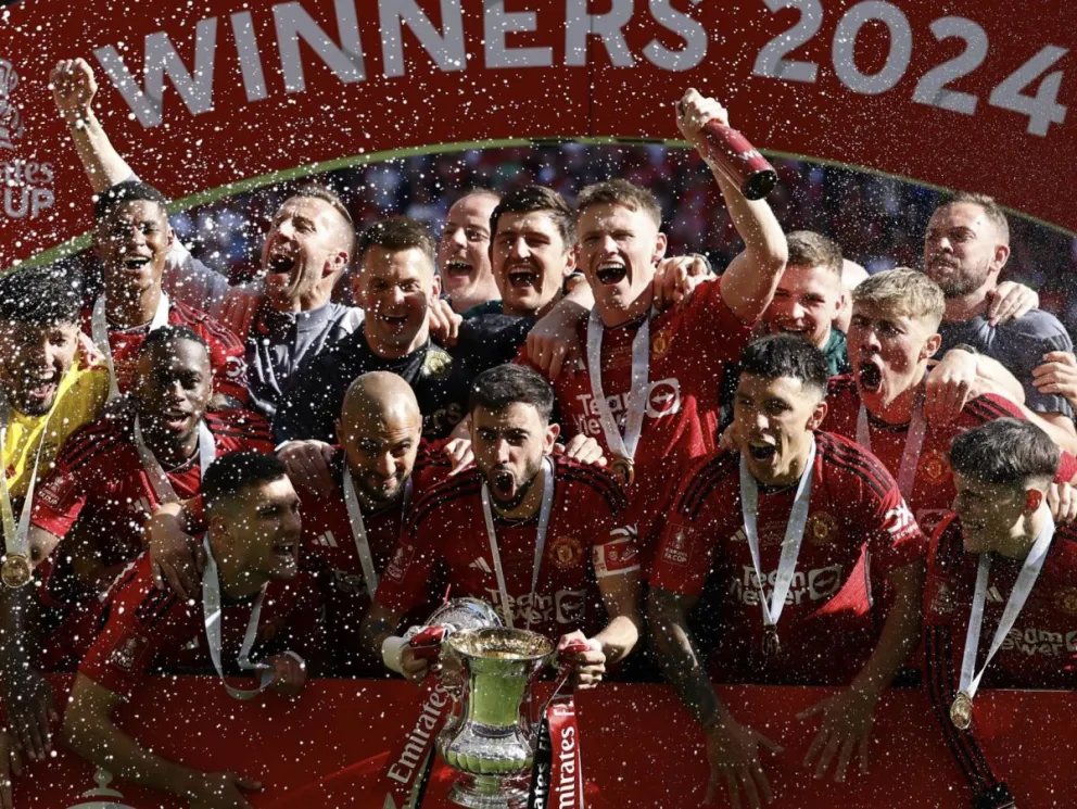 Jugadores del Manchester United, el capitán Bruno Fernandes aparece en el centro agarrando el trofeo, festejan el título. Foto: EFE