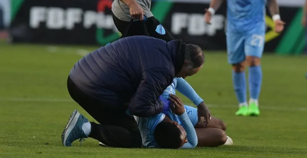 Quinteros tirado en el césped por su hombro mientras lo revisa el doctor Aponte. Foto: APG.