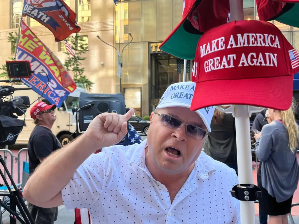 Un seguidor del expresidente Donald Trump grita consignas frente a una cámara mientras sostiene una gorra de 'Haz a los Estados Unidos grande otra vez' a las afueras del edificio de la Torre Trump este viernes, en Nueva York (EEUU). Foto: EFE