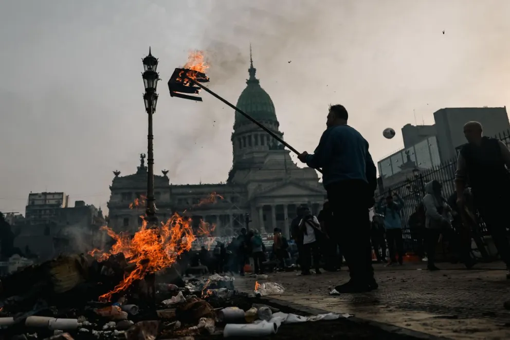 Un hombre quema una caja durante enfrentamientos entre la policía y personas que protestan a las afueras del Senado, este 12 de junio de 2024, en Buenos Aires. Foto: EFE