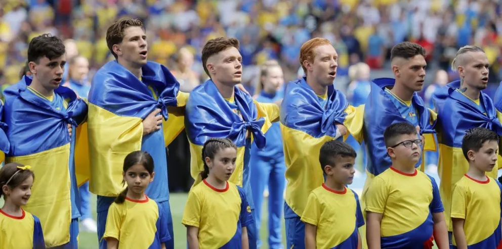 Los jugadores de la selección ucraniana con la bandera de su país atada al cuello entonan el himno nacional. Foto: EFE.