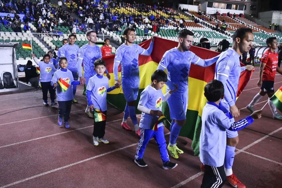 Jugadores del club Bolívar ingresan con la bandera nacional a un partido del torneo local. Foto: APG