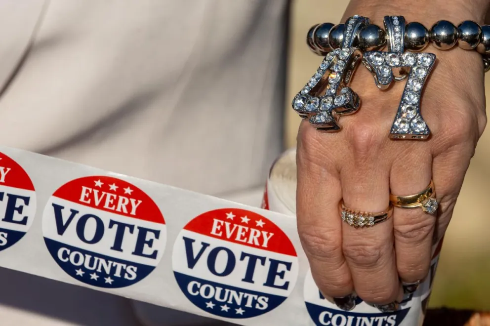 Un partidario de Trump que lleva una pulsera con la leyenda "47" sostiene pegatinas con la leyenda "Cada voto cuenta" fuera de un centro de votación el día de las elecciones en Filadelfia, Pensilvania. Foto: EFE