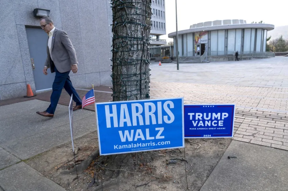 Un hombre camina frente a unos carteles de los candidatos presidenciales, los demócratas Harris y Walz y los republicanos Trump y Vance, en un centro de votación. Foto: EFE