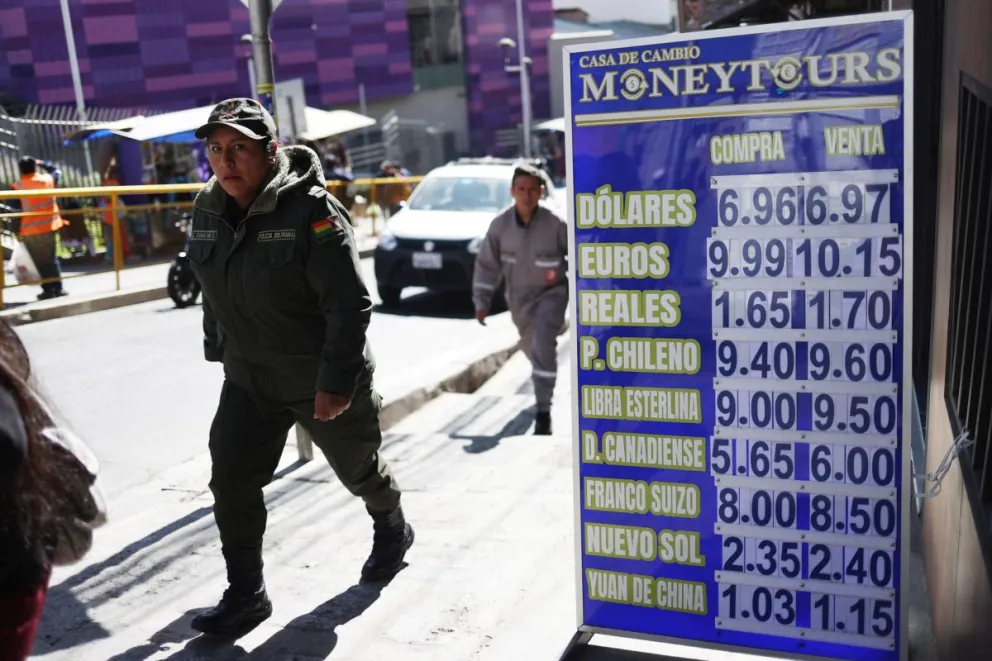Personas caminando frente a un cartel en el que se observan los precios de una casa de cambio, en La Paz. Foto: EFE