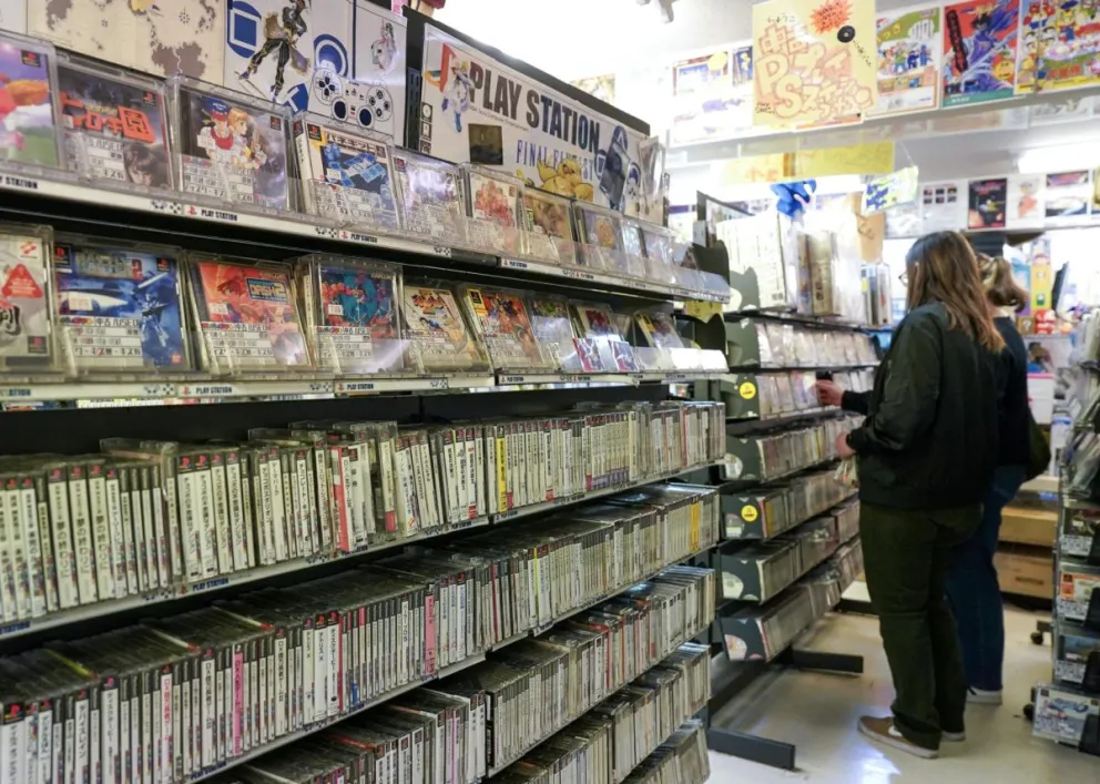 Unas personas frente a una estantería con juegos "retro" de PlayStation en Tokio. Foto: EFE