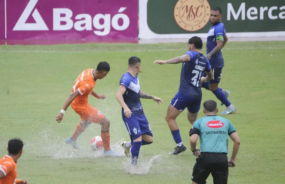 Ricardo Cadima, jugador de Pari, conduce con dificultad el balón por el agua en el campo, mientras los jugadores de G salen a su marca. Foto: APG