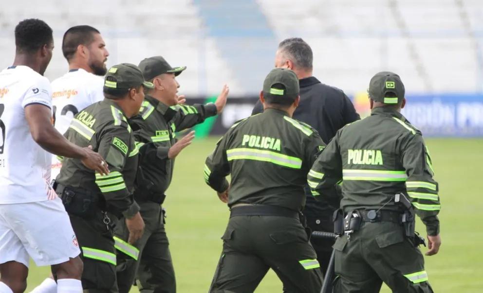 De la torre (camisa negra) se retira de la cancha rodeado de efectivos policiales. Dos de sus jugadores se acercan a cuidarlo. Foto: APG