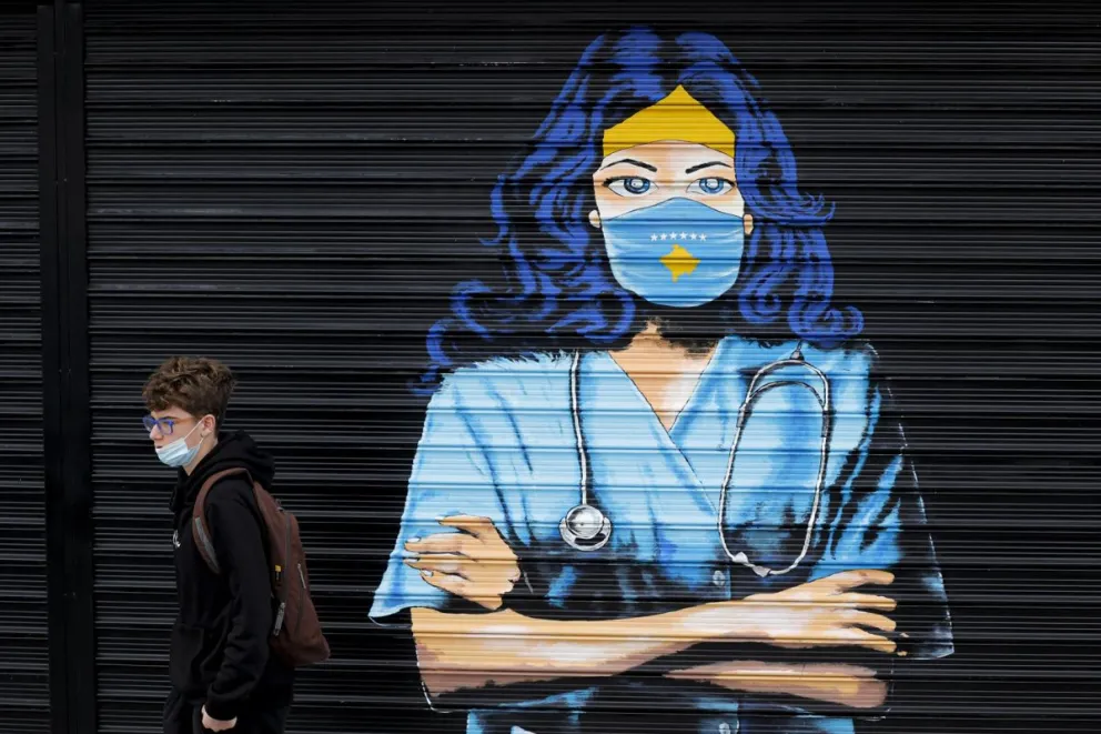 Un chico con mascarilla pasa delante de un mural en Pristina - imagen de archivo. Foto: EFE
