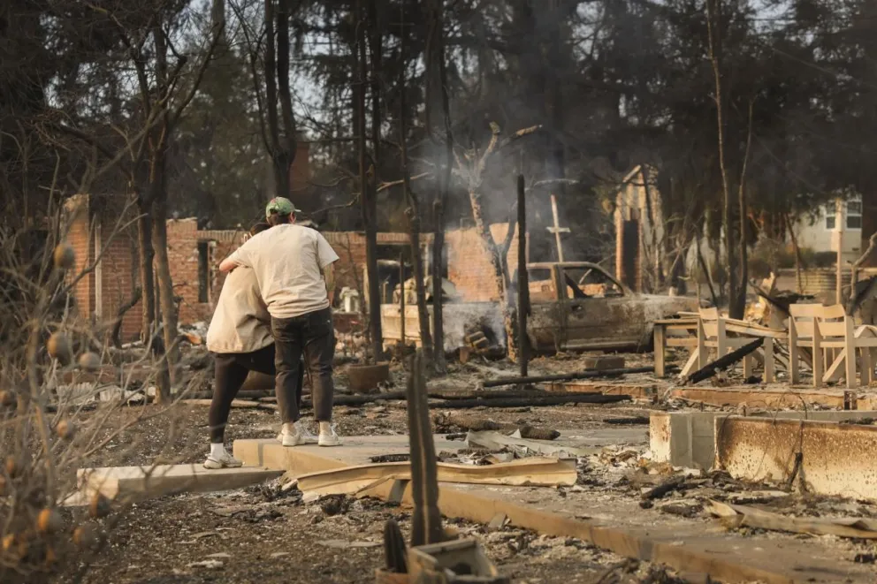 Personas se abrazan mientras contemplan los restos de una casa destruida por el incendio forestal de Eaton en Altadena, California. Foto: EFE