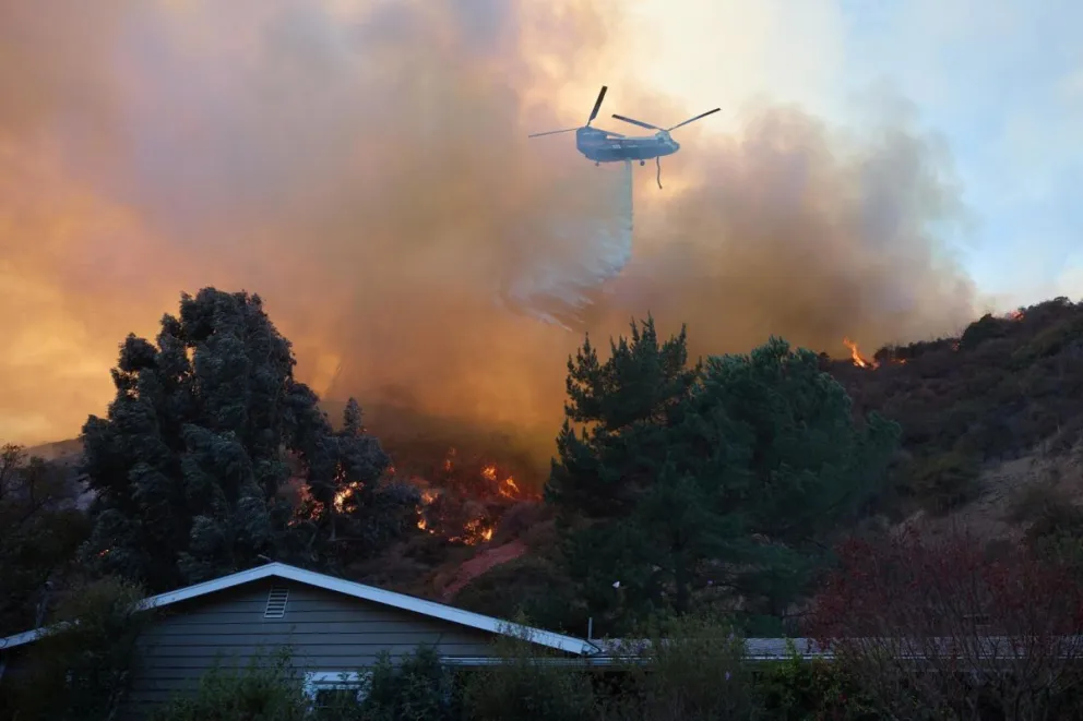 Un helicóptero arroja agua sobre una casa durante el incendio forestal de Palisades en Los Ángeles. Foto: EFE