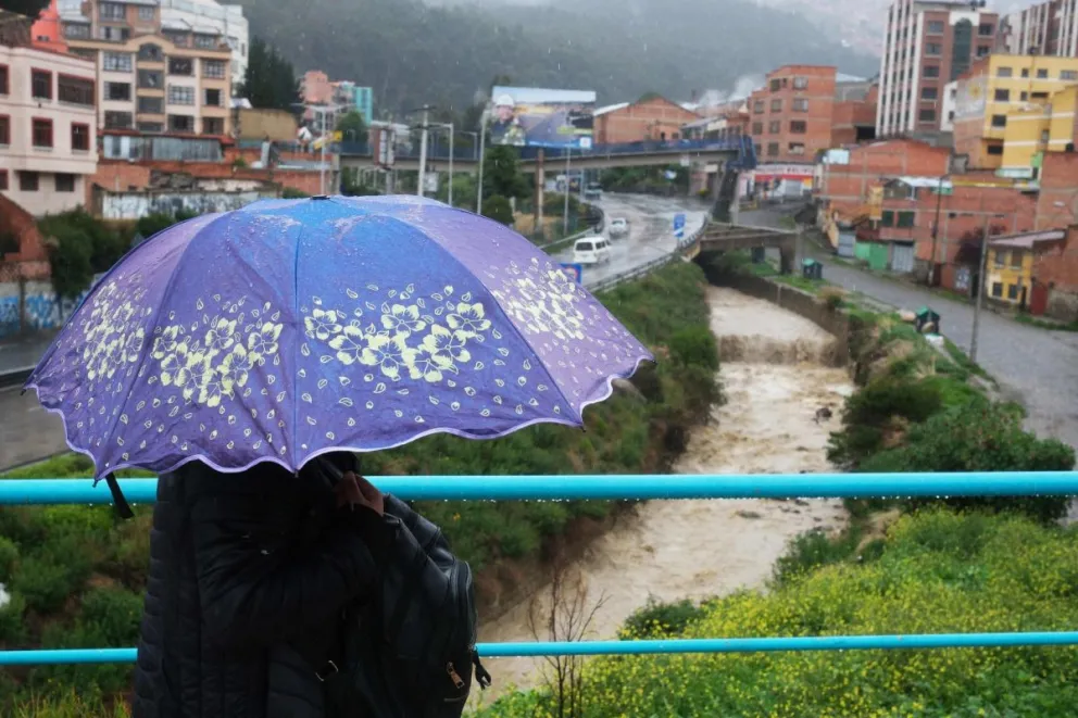 Fotografía de archivo en donde una mujer lleva un paraguas en inmediaciones de un río durante una jornada de lluvias en La Paz (Bolivia). Foto: EFE