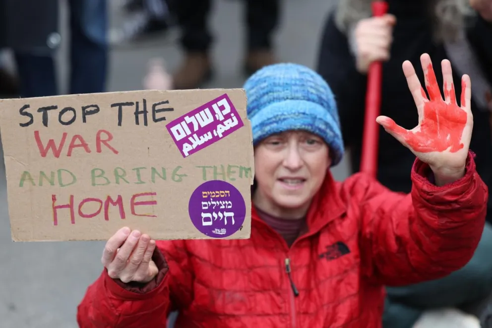Una manifestante con pintura roja en las manos sostiene un cartel que pide detener la guerra en Gaza. Foto: EFE