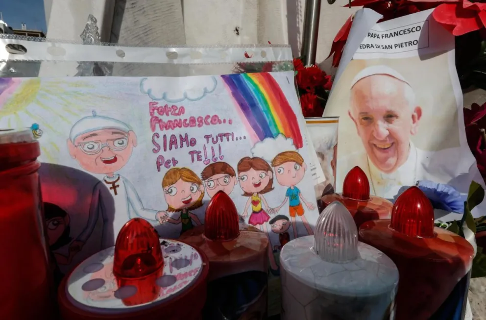 Un dibujo y una fotografía del papa Francisco bajo la estatua de Juan Pablo II, frente al Hospital Agostino Gemelli. Foto: EFE