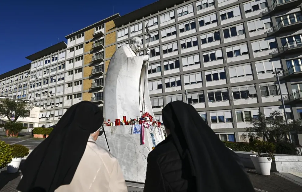 Monjas rezan frente a la estatua del Papa Juan Pablo II en la entrada del Hospital Gemelli, donde está hospitalizado el Papa Francisco. Foto: EFE 