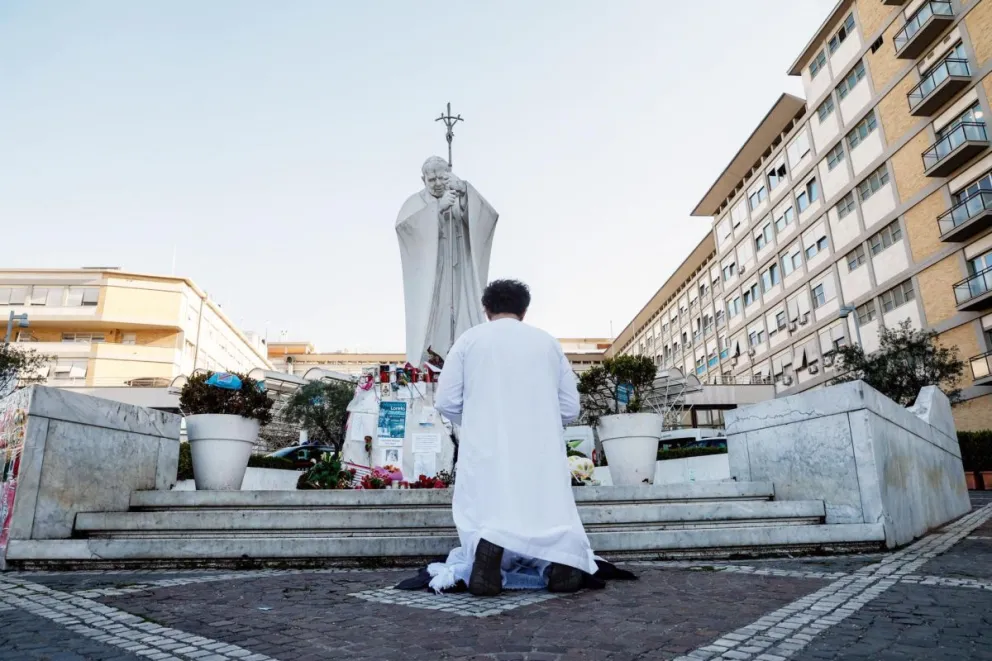 Una persona reza cerca de la estatua de Juan Pablo II frente al hospital, donde el Papa Francisco continúa su tratamiento por neumonía bilateral, en Roma. Foto: EFE
