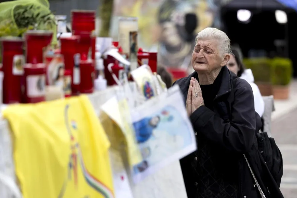 Una persona mayor reza junto a velas por el Papa Francisco en la estatua del Papa Juan Pablo II, frente al Hospital Gemelli, en Roma, Italia. Foto: EFE