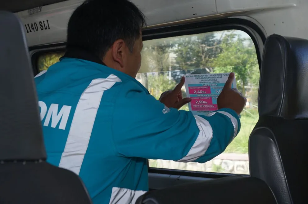 Un funcionario de la Alcaldía pega un adhesivo con las tarifas en un minibús. Foto: APG