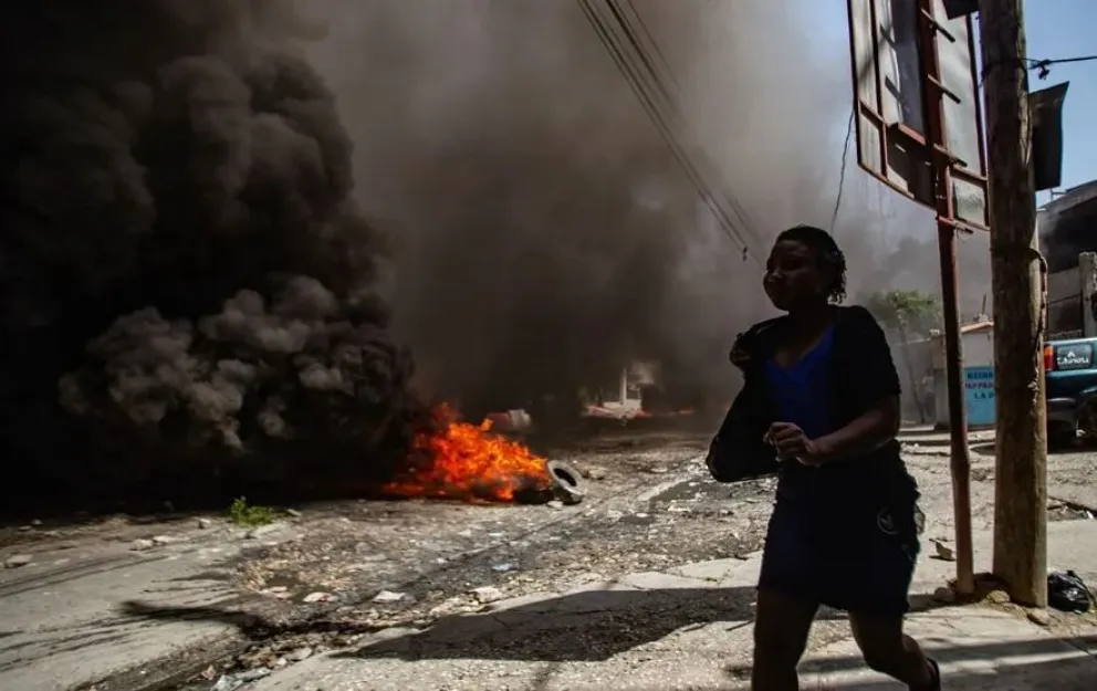 Una mujer camina frente una barricada con fuego en Haití, país que atraviesa una crisis de violencia. Foto: EFE