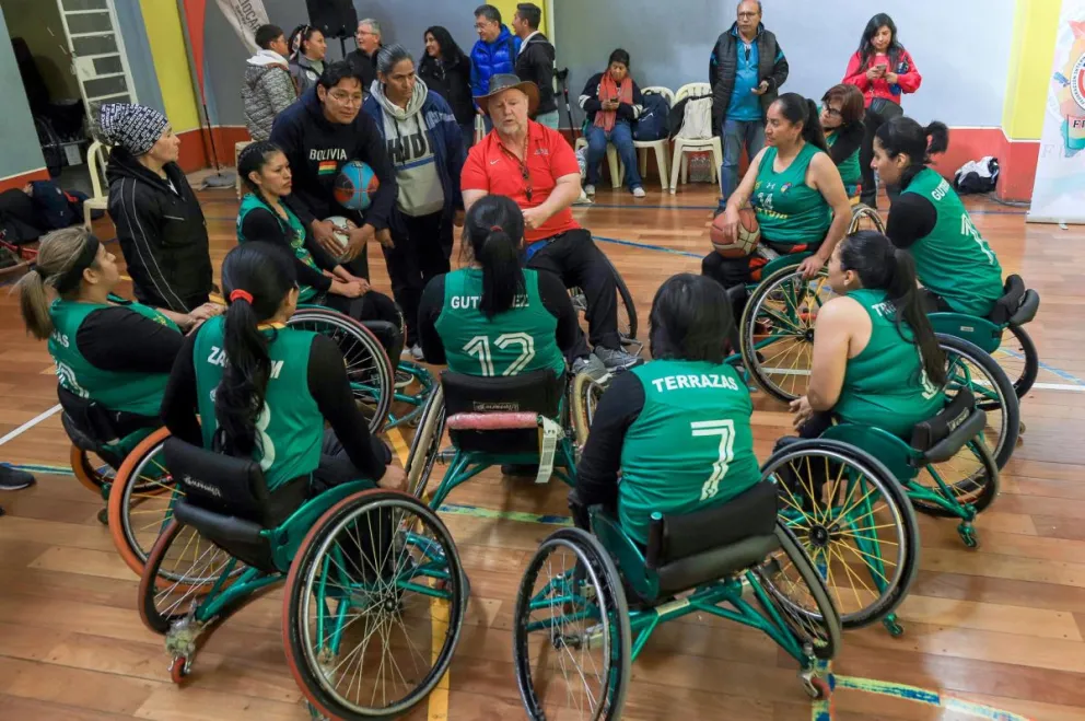 El entrenador Hughes (de rojo) habla con las seleccionadas de Bolivia. Foto: EFE.