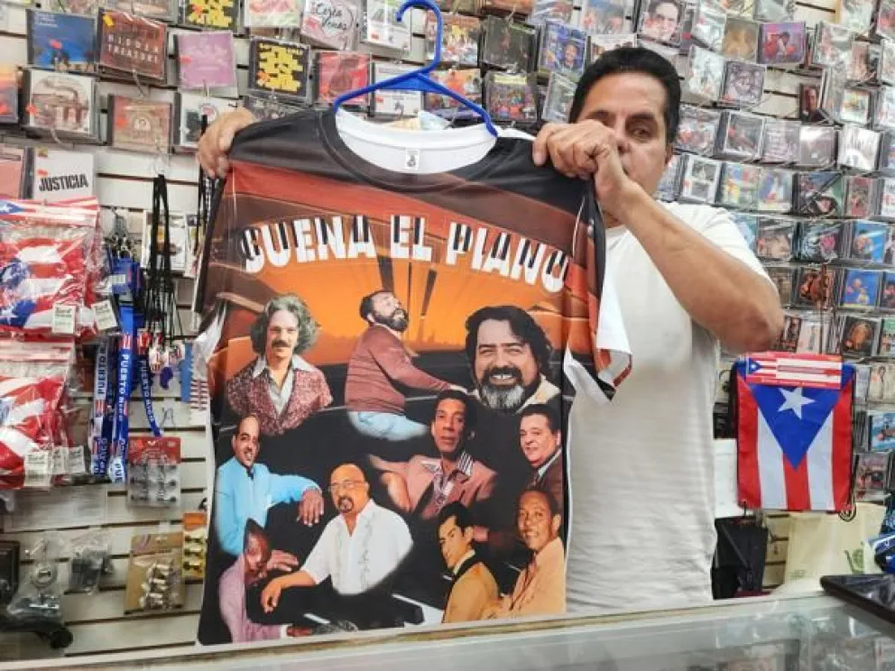El dueño del local 'El Barrio Music Center', Reynaldo Meléndez, fue captado este jueves, 7 de agosto, al sostener una camiseta con una imagen de Eddie Palmieri rodeado de otros pianistas, en su local, en Nueva York (NY, EE.UU.). EFE/Ruth Hernández