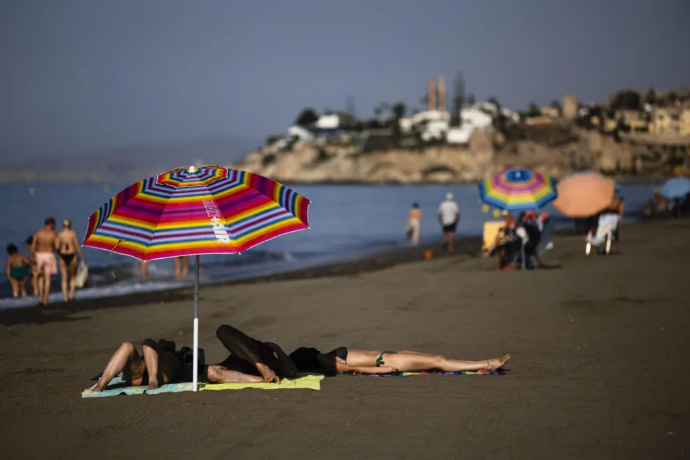 Varias personas se resguardan del sol baja una sombrilla en la playa del Rincón de la Victoria (Málaga). Foto: EFE 