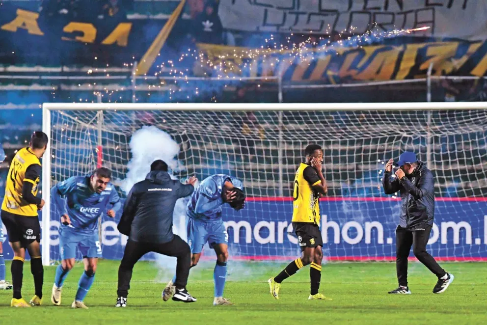 Jugadores de The Strongest y Blooming, y miembros de los cuerpo técnicos tratan de protegerse de las bengalas lanzadas por los hinchas atigrados desde la curva sur. Foto: APG