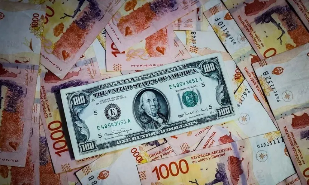 Billetes de pesos argentinos y un billete de 100 dólares estadounidenses. Foto: EFE