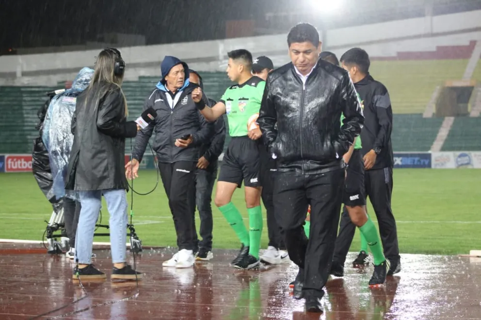 El árbitro del partido, Gabriel Mendoza, conversa con Mauricio Soria, DT de Blooming, en medio de la torrencial lluvia. 