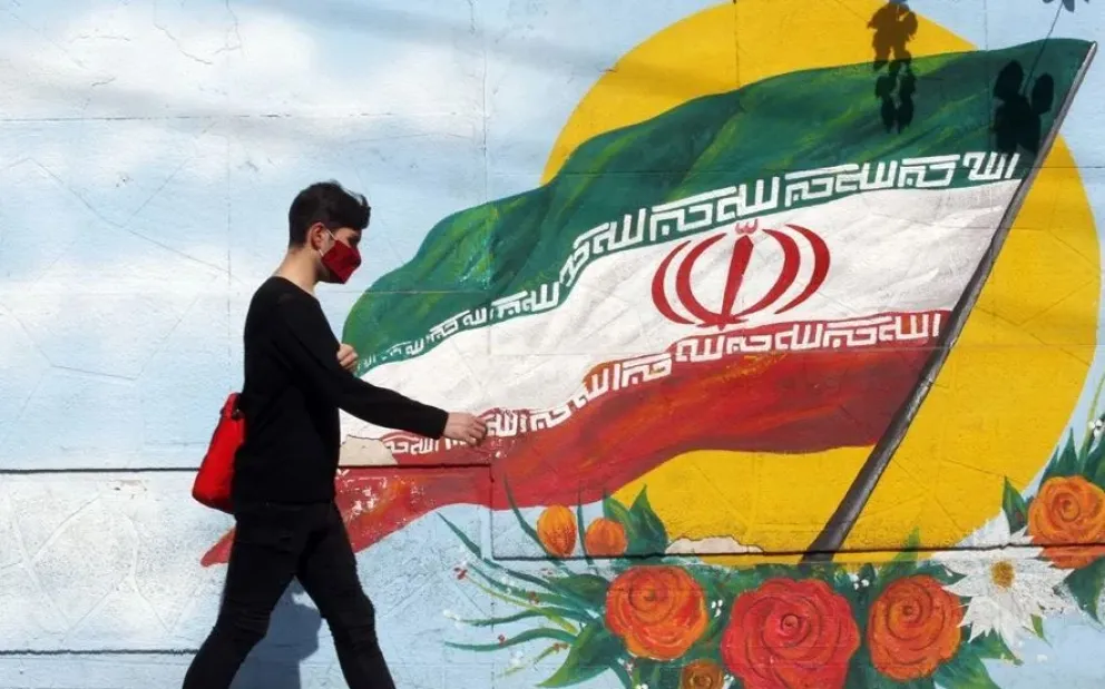 Un hombre que camina frente a un muro con la bandera de Irán, en una imagen de archivo. Foto: EFE