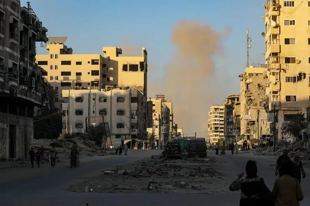 Palestinos se desplazan por la calle Al Jalaa mientras se eleva el humo tras un ataque aéreo israelí en la ciudad de Gaza. Foto: EFE