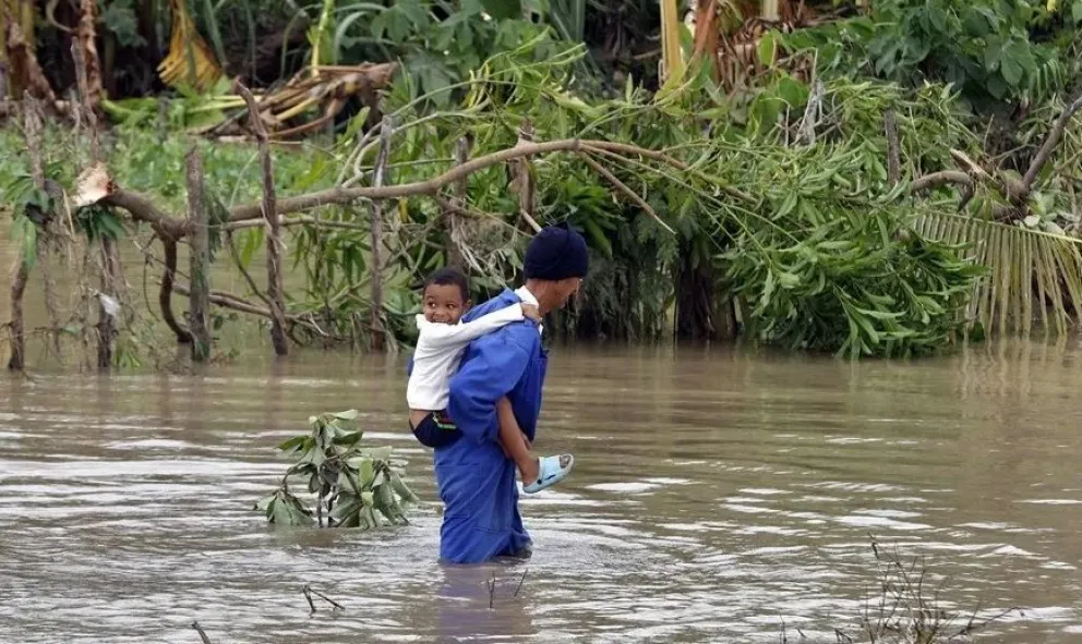 Un hombre cruza un río crecido cona un niño en el poblado de Guama en Santiago de Cuba. Foto: EFE
