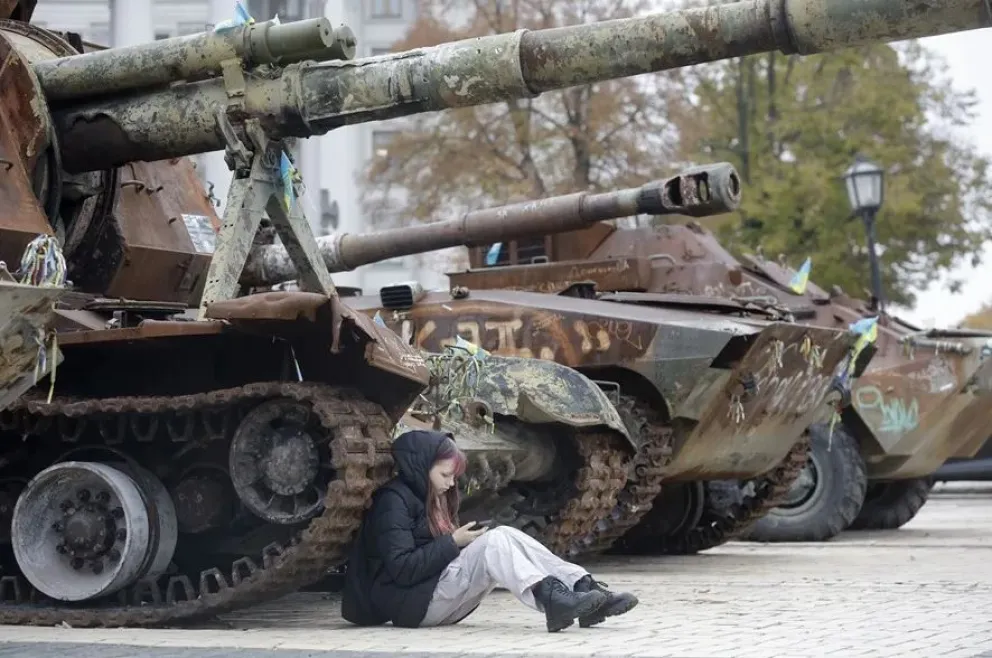 Una ucraniana consulta su teléfono móvil sentada junto a tanques en Kiev. Foto: EFE