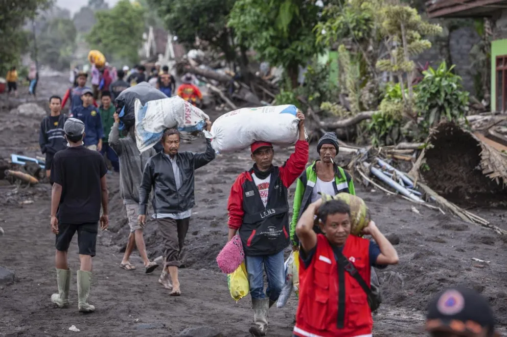 Un grupo de gente traslada sus pertenecias tras el anuncio de evacuación, en uno de los sitios afectados por la erupción del volcán Semeru. Foto: EFE.