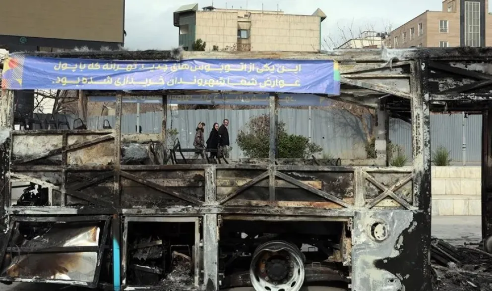 Iraníes caminan junto a los restos de un autobús público incendiado en Teherán el jueves. Foto: EFE