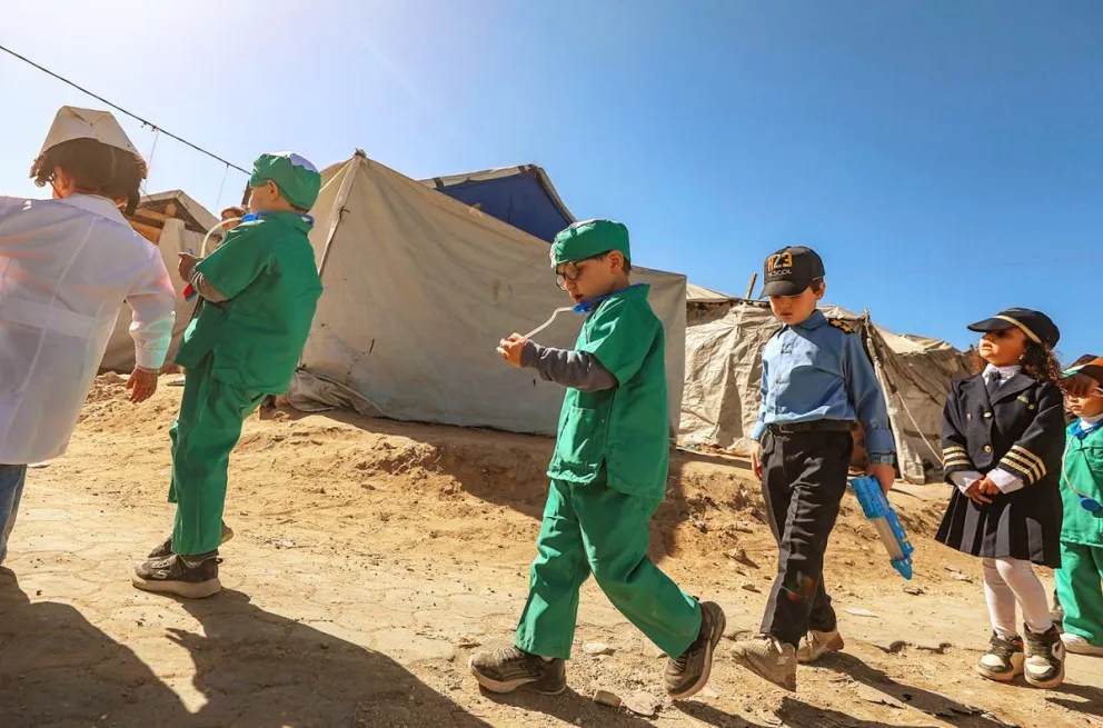 Niños palestinos del Colegio Internacional Británico, vestidos como médicos y trabajadores de la defensa civil, caminan cerca de las ruinas de edificios destruidos en la Ciudad de Gaza. Foto: EFE