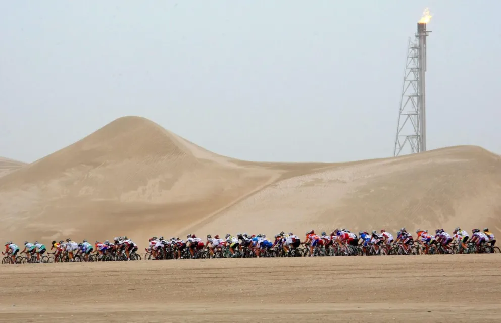 Pelotón de ciclistas pasa junto a una fábrica de gas en el desierto. Foto: Archivo / EFE