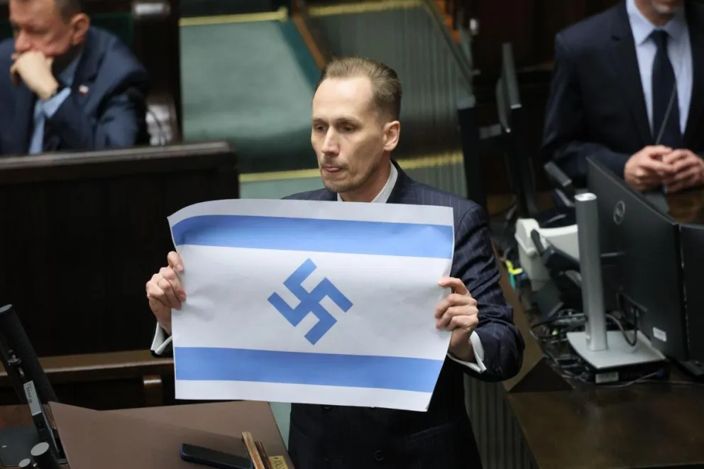 El diputado del partido polaco de extrema derecha Confederación muestra una bandera israelí marcada con una esvástica en el Parlamento polaco, el 14 de abril, cuando acusó a Israel de ser el "nuevo Tercer Reich".  