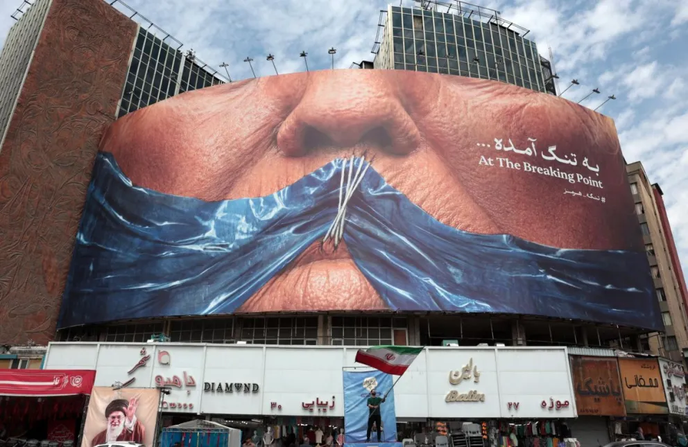 Un iraní sostiene la bandera nacional de Irán frente a una enorme valla publicitaria antiestadounidense que hace referencia al presidente de EE. UU. Donald Trump y al estrecho de Ormuz, el 2 de mayo en la plaza Valiasr de Teherán, Irán. Foto: EFE
