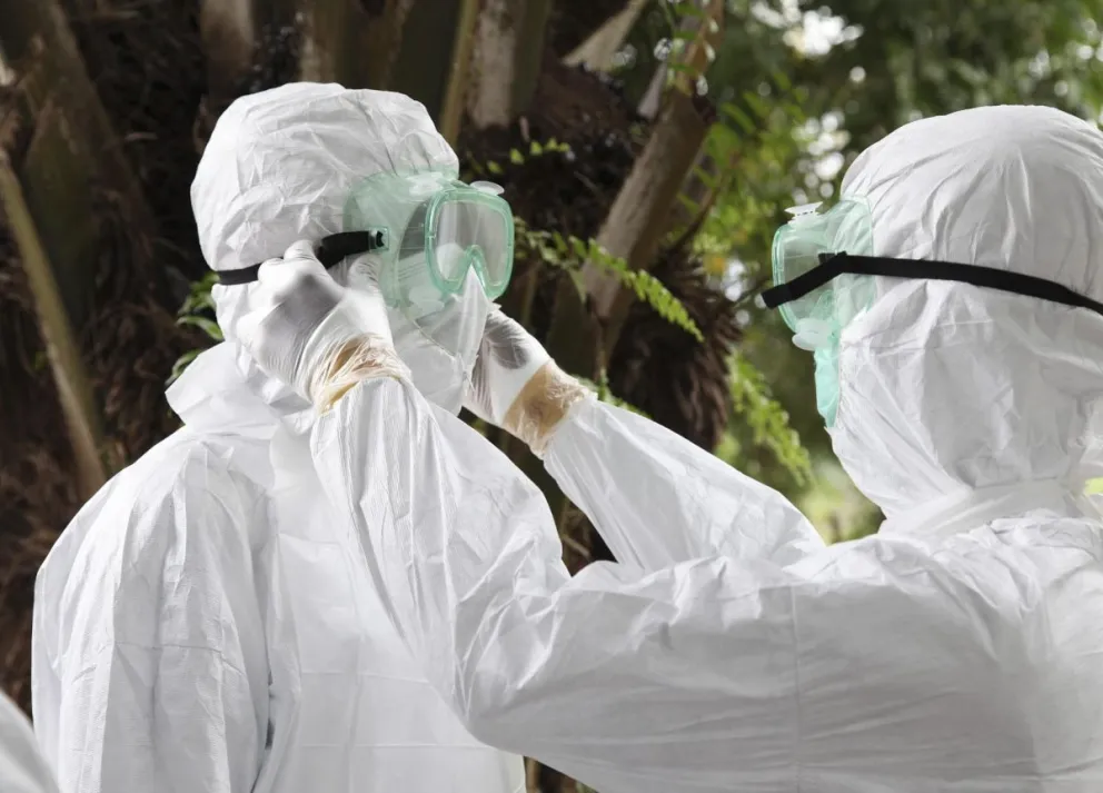 Dos enfermeros liberianos mientras revisan sus equipos de protección individual antes de transportar el cuerpo de una víctima del ébola para su entierro. Foto: EFE