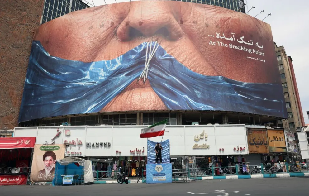 Un hombre sostiene la de Irán delante de una gran valla publicitaria antiestadounidense con un montaje del presidente de Estados Unidos Donald Trump y el estrecho de Ormuz, el 28 de mayo en la plaza Valiasr de Teherán, Irán. Foto: EFE