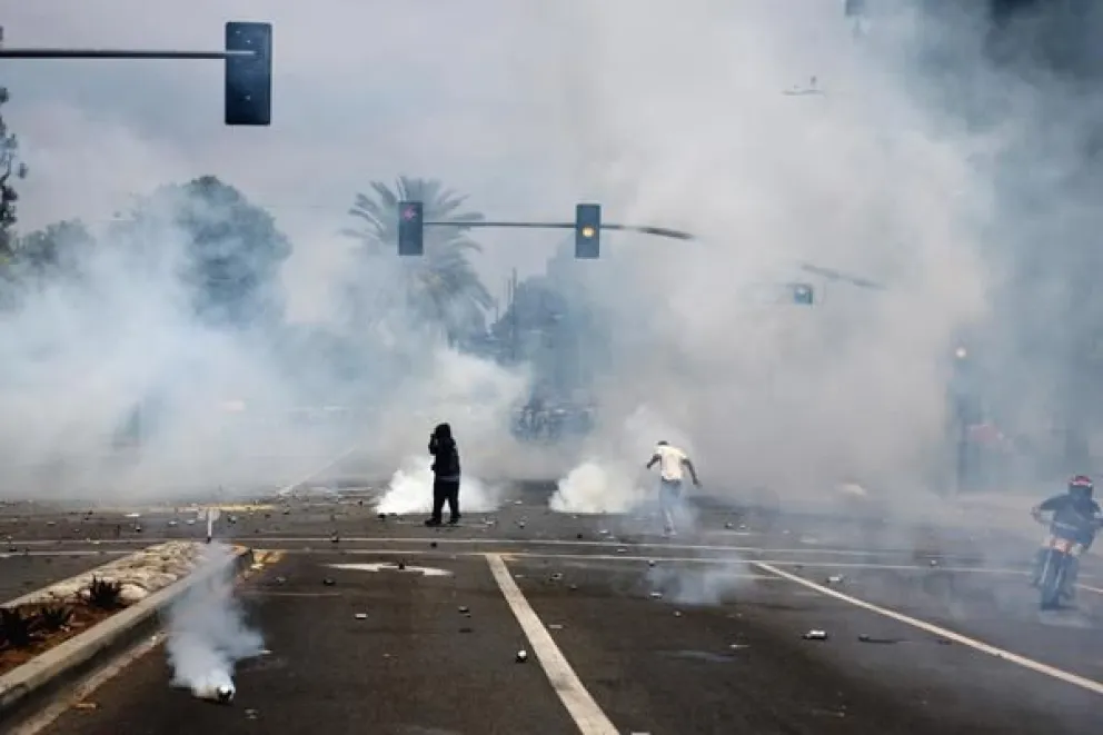 Manifestantes corren a través del gas lacrimógeno lanzado por agentes federales cerca de un Home Depot después de que el Servicio de Inmigración y Control de Aduanas (ICE) realizara una redada en Paramount, California. Foto: EFE