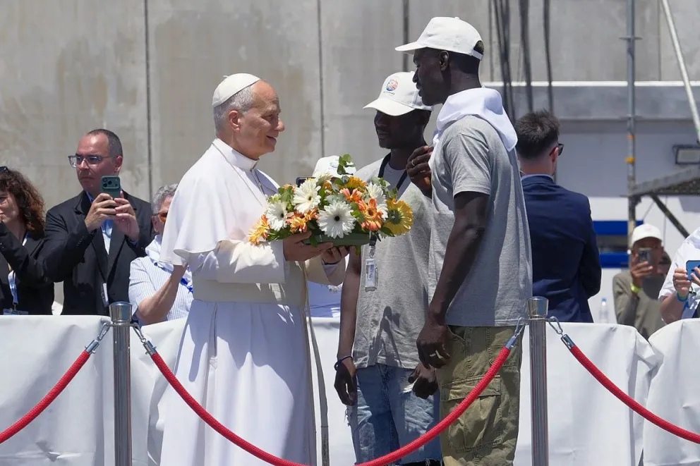 El papa León XIV recibe flores de dos voluntarios para protagonizar una ofrenda floral en el mar en recuerdo de los migrantes muertos en la travesía durante el encuentro con más de un millar de inmigrantes de África. Foto: EFE