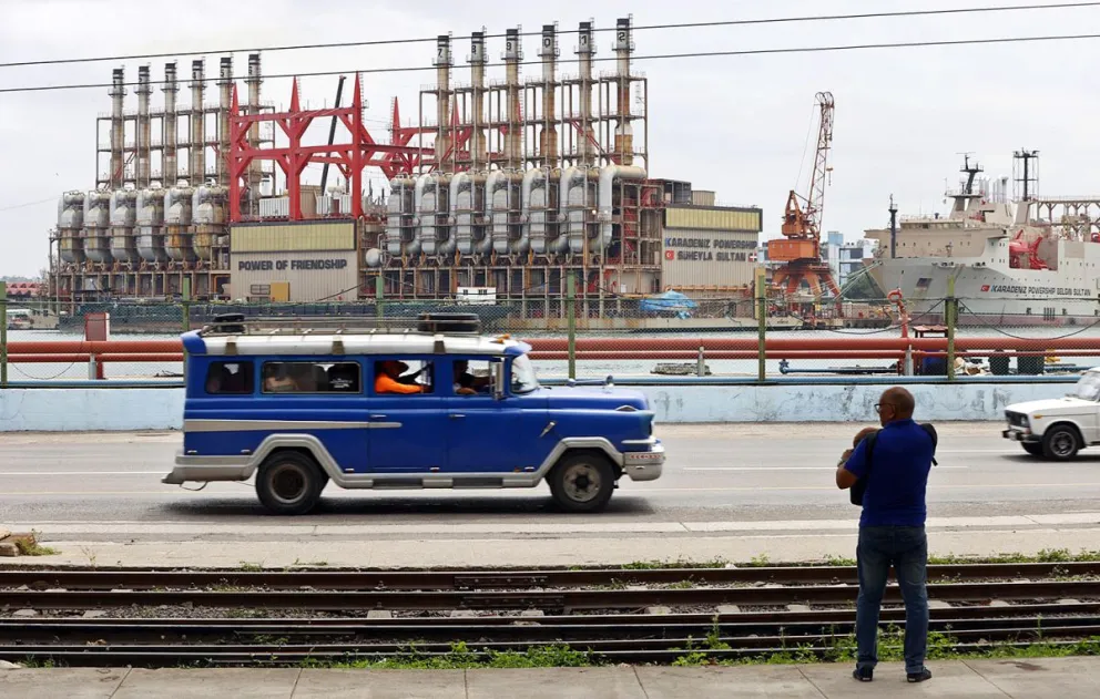 Foto de archivo, un auto viejo de transporte colectivo al pasar frente a una planta flotante de generación eléctrica en el puerto de La Habana (Cuba). Foto: EFE