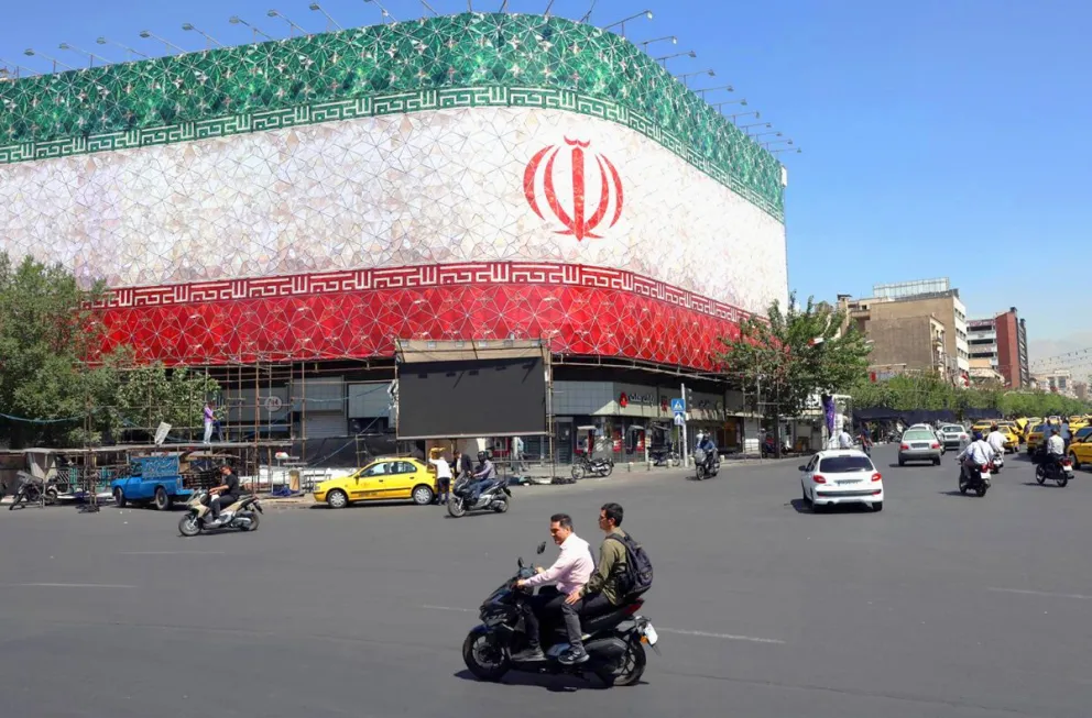 Unos iraníes pasan en coche junto a una valla publicitaria con la bandera nacional de Irán en la plaza Enqelab de Teherán, Irán. Foto: EFE