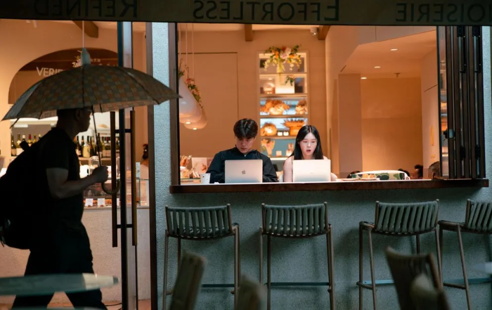 Personas mirando sus computadores portátiles mientras otra camina por una calle de Shanghái, China. Foto: EFE