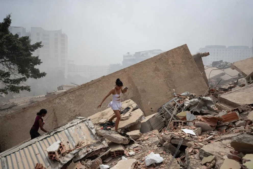 Personas caminan este jueves, entre los escombros de edificios afectados por los terremotos en La Guaira (Venezuela). Foto: EFE