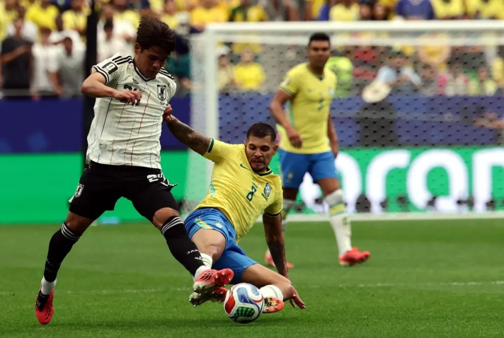 Bruno Guimarães, de Brasil, le saca desde el suelo la pelota al japonés Kaishu Sano. Foto: EFE
